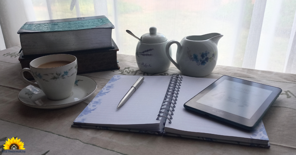 Real homemaking scene with books, tea, journal, and Kindle by a sunlit window